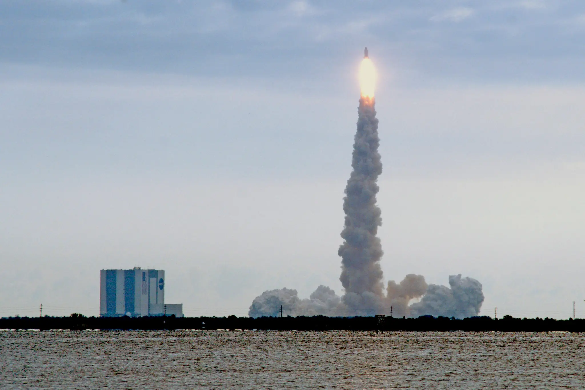 Long-exposure of a rocket launch lifting from a Florida pad, smoke trail rising into a hazy sky